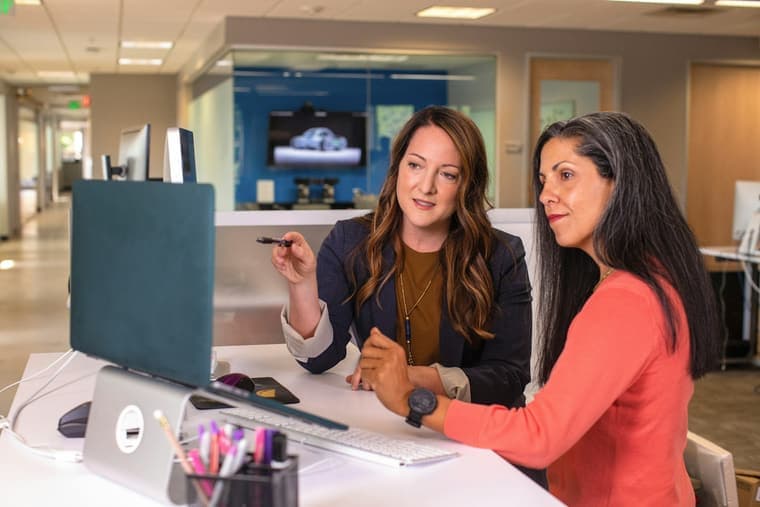 Two people at a desk going through an application on a laptop